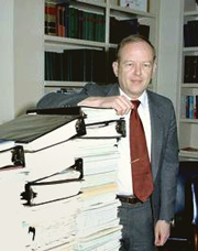 Assistant Secretary of Defense (Comptroller) Jack Borsting standing by several large stacks of books and reports.